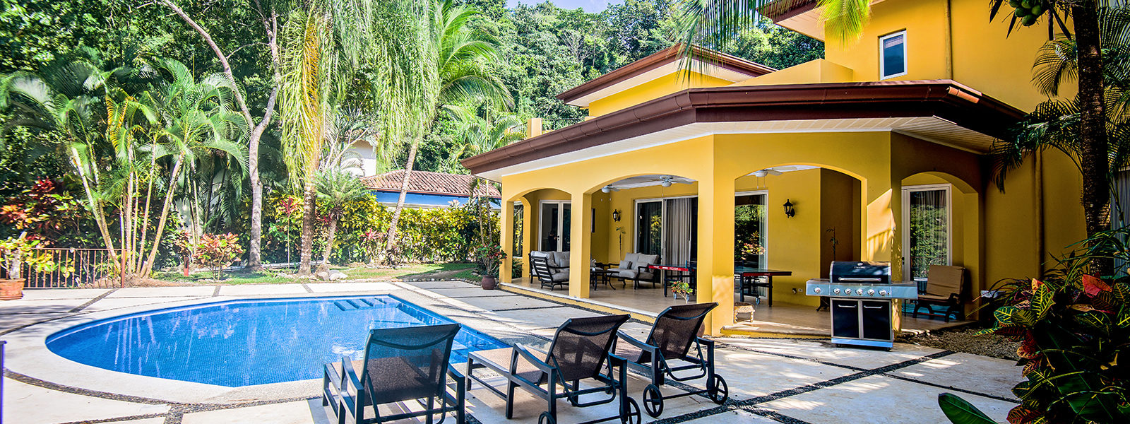This lavish vacation home in Jaco offers a sun-drenched pool and patio with vibrant natural surroundings.